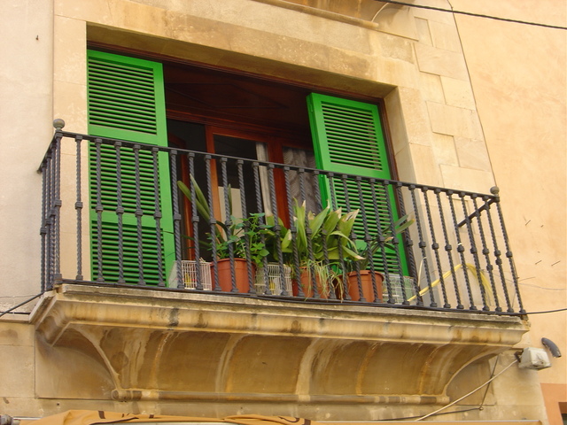 Balkón s nerezovým zábradlím, zelenými dverami a kvetmi.jpg